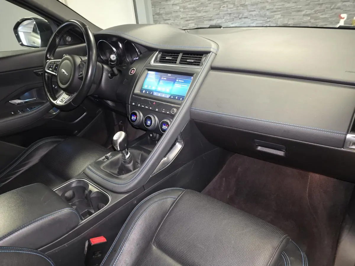 Intérieur Jaguar E-PACE D150 gris, vue côté passager avec console centrale et volant cuir multifonction.