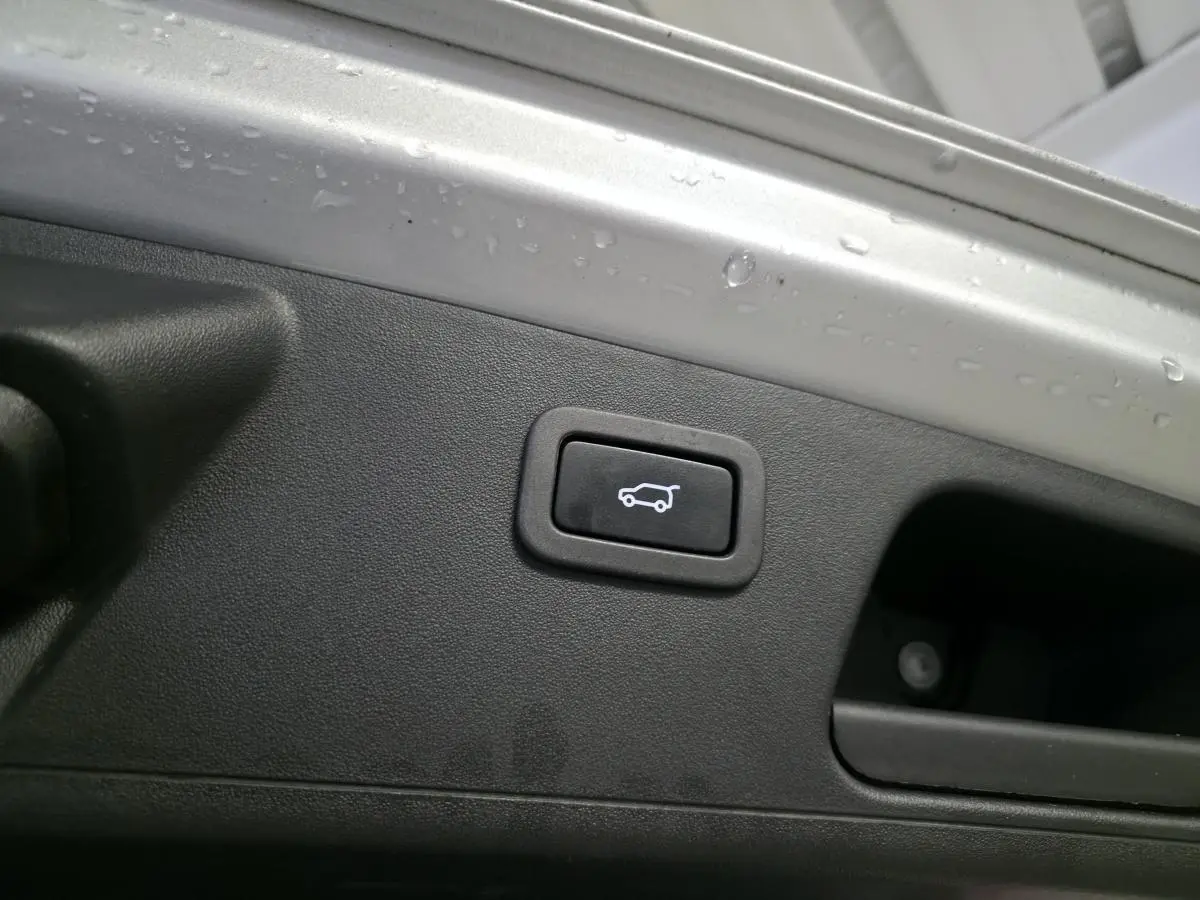 Bouton d'ouverture électrique du hayon sur la partie intérieure grise du coffre d'un Jaguar E-PACE gris.