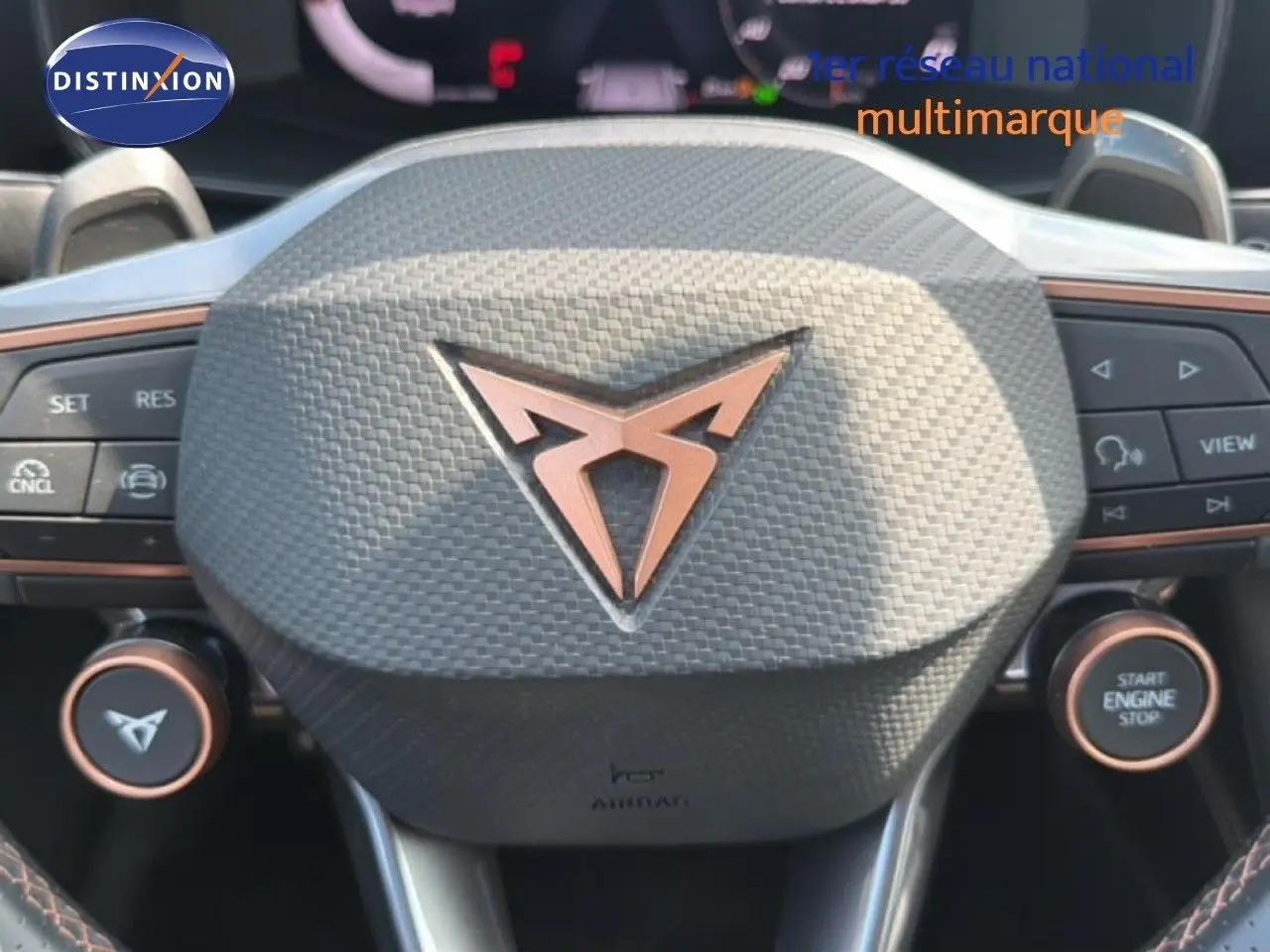 Gros plan sur le volant gris texturé avec logo CUPRA cuivré, boutons multifonctions et démarrage moteur visible.