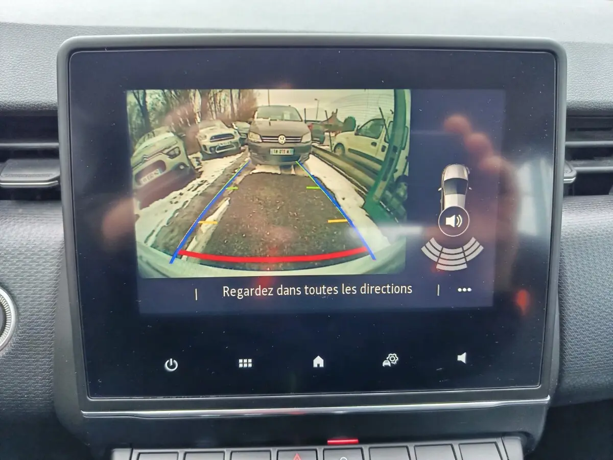 Écran tactile intérieur montrant la caméra de recul avec vue arrière et lignes de guidage colorées sur route enneigée.