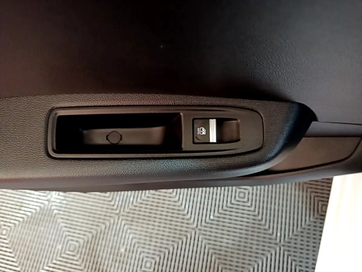 Gros plan sur le bouton de commande de la vitre électrique côté porte intérieure d’une Renault Clio Business blanche.