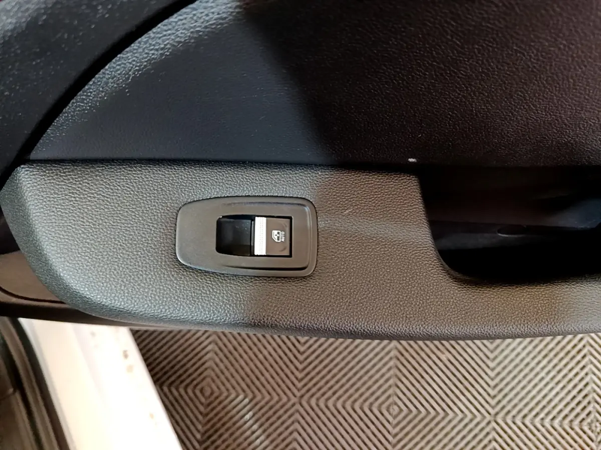 Gros plan sur le bouton de commande de la vitre électrique côté conducteur d’une Renault Clio blanche, intérieur noir.