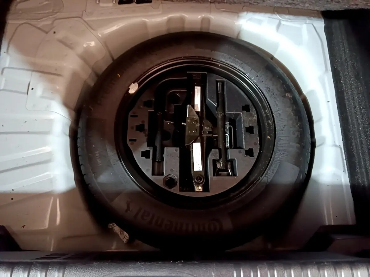 Vue plongeante sur la roue de secours noire et ses outils dans le coffre blanc d'une Renault Clio Business TCe 100 essence 2020.