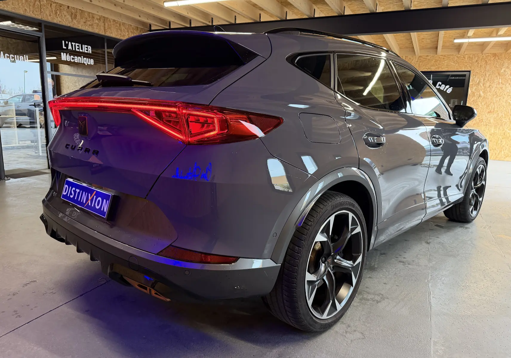 Vue 3/4 arrière droite d’un CUPRA Formentor gris 2023, avec feux arrière allumés et jantes noires distinctives.