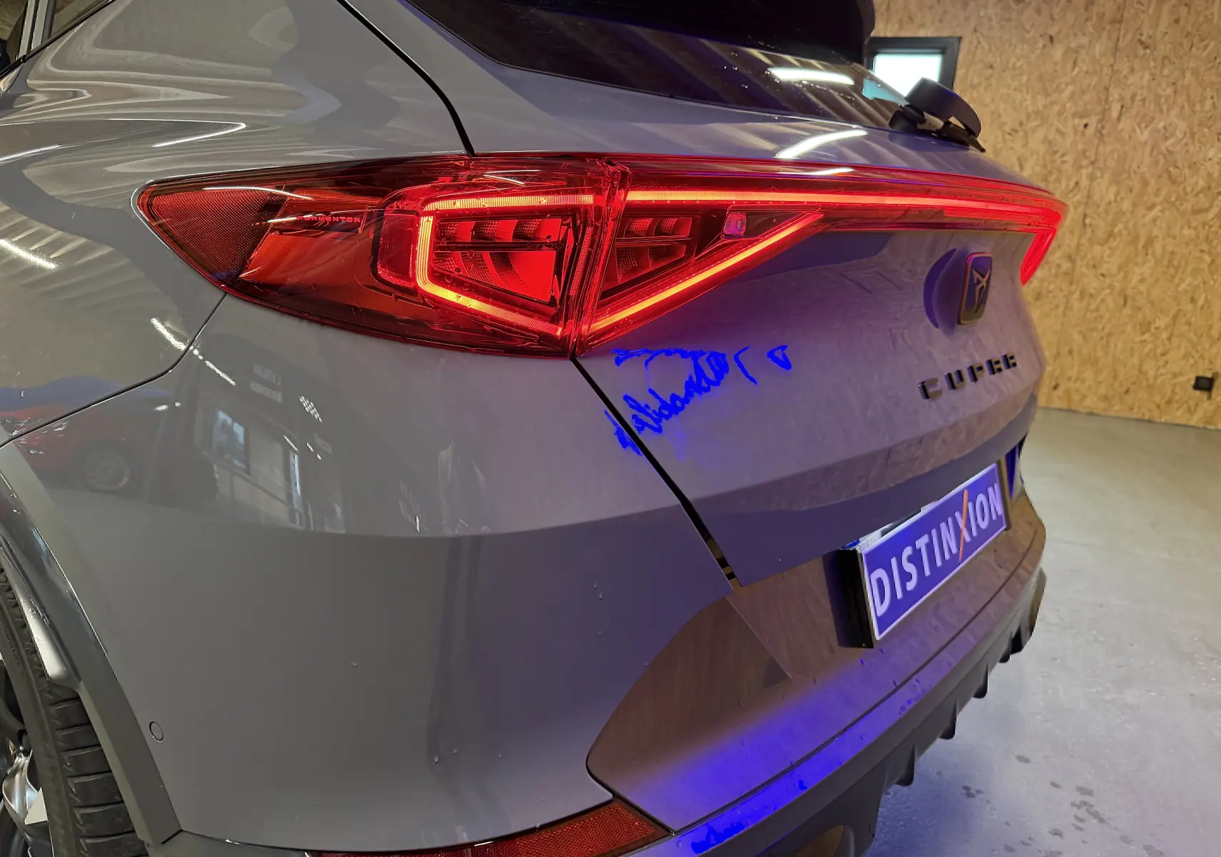 Vue 3/4 arrière droite d'une CUPRA Formentor gris avec feux arrière allumés et logo distinctif sur le hayon.