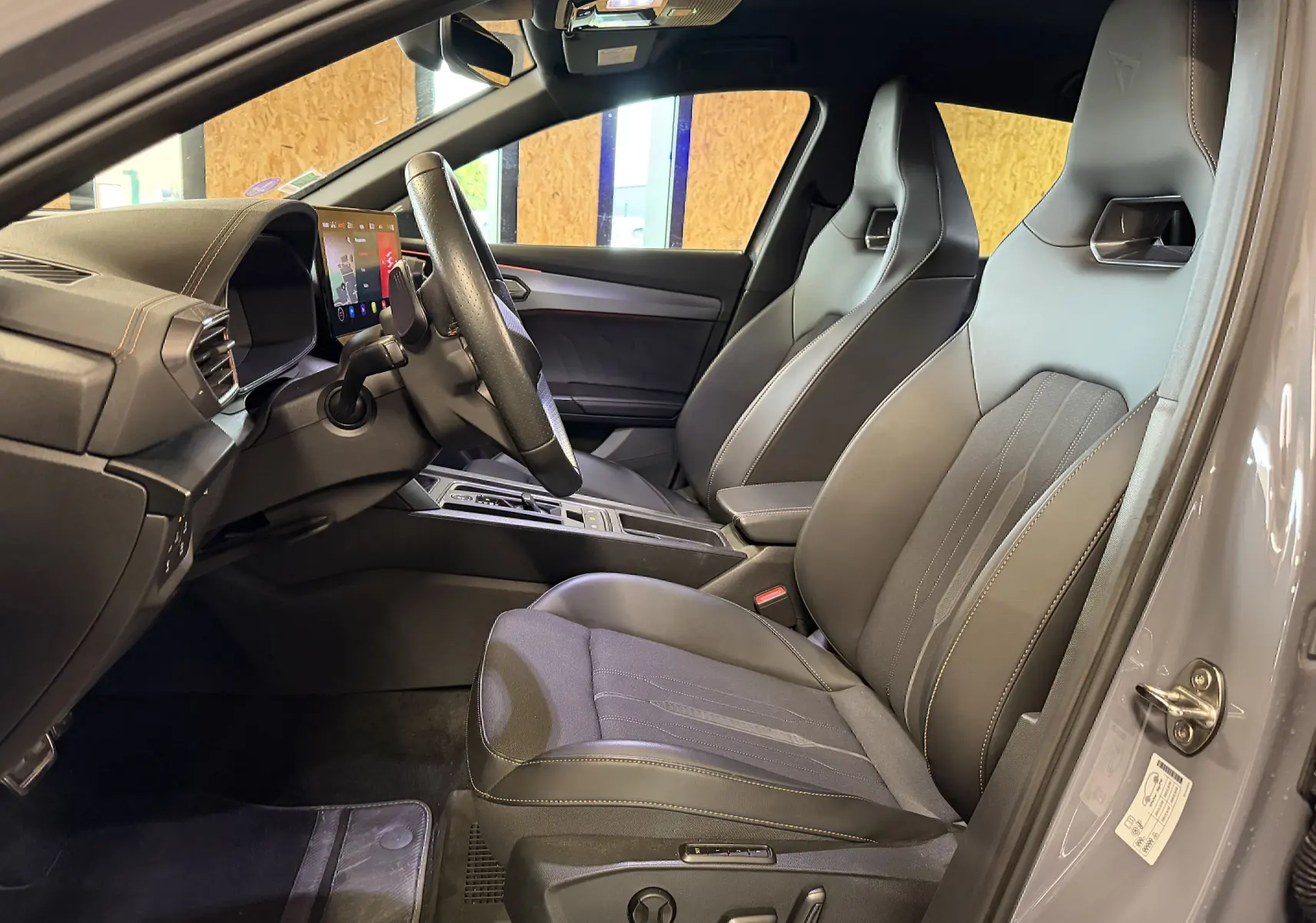 Vue intérieure côté conducteur du CUPRA Formentor gris 2023, mettant en valeur les sièges sport en cuir et tissu avec surpiqûres contrastées.