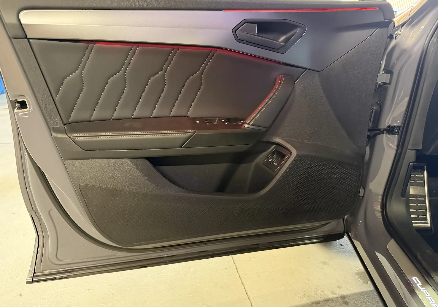 Vue intérieure de la porte avant gauche grise du CUPRA Formentor 1.4 Hybrid 245 VZ avec surpiqûres rouges et commandes électriques.