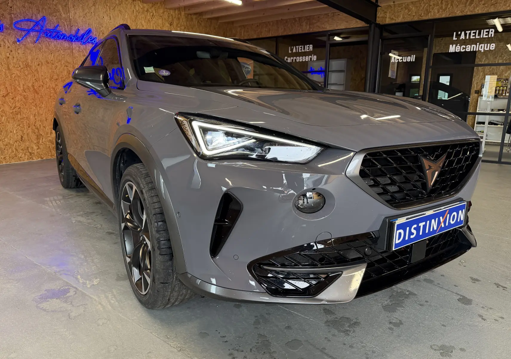 Vue 3/4 avant gauche d'un CUPRA Formentor gris 2023 avec calandre noire et phares LED, en intérieur showroom.