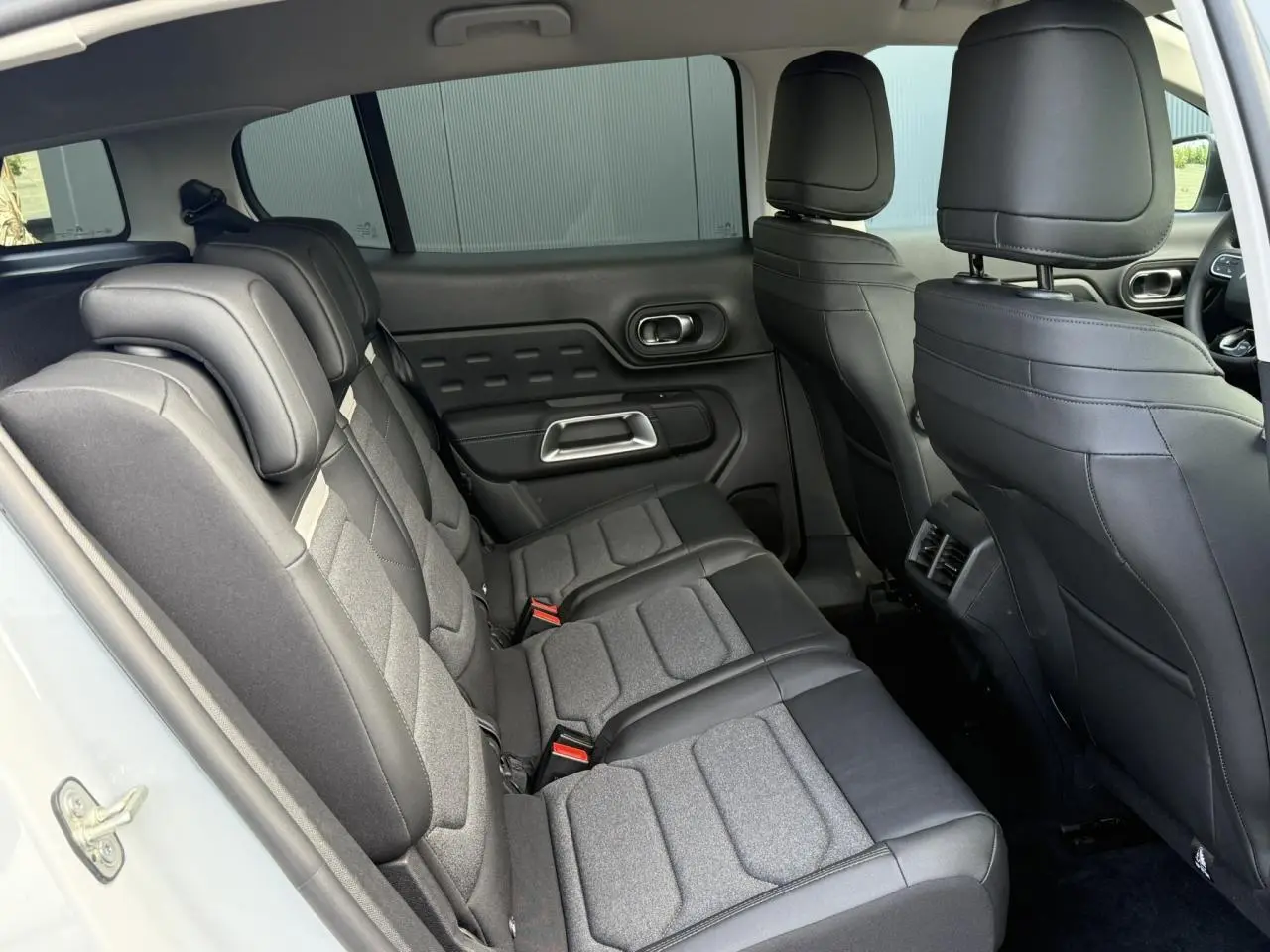 Vue intérieure côté gauche des sièges arrière en tissu et cuir noir du Citroën C5 Aircross blanc Okenite, avec appuie-têtes réglables.