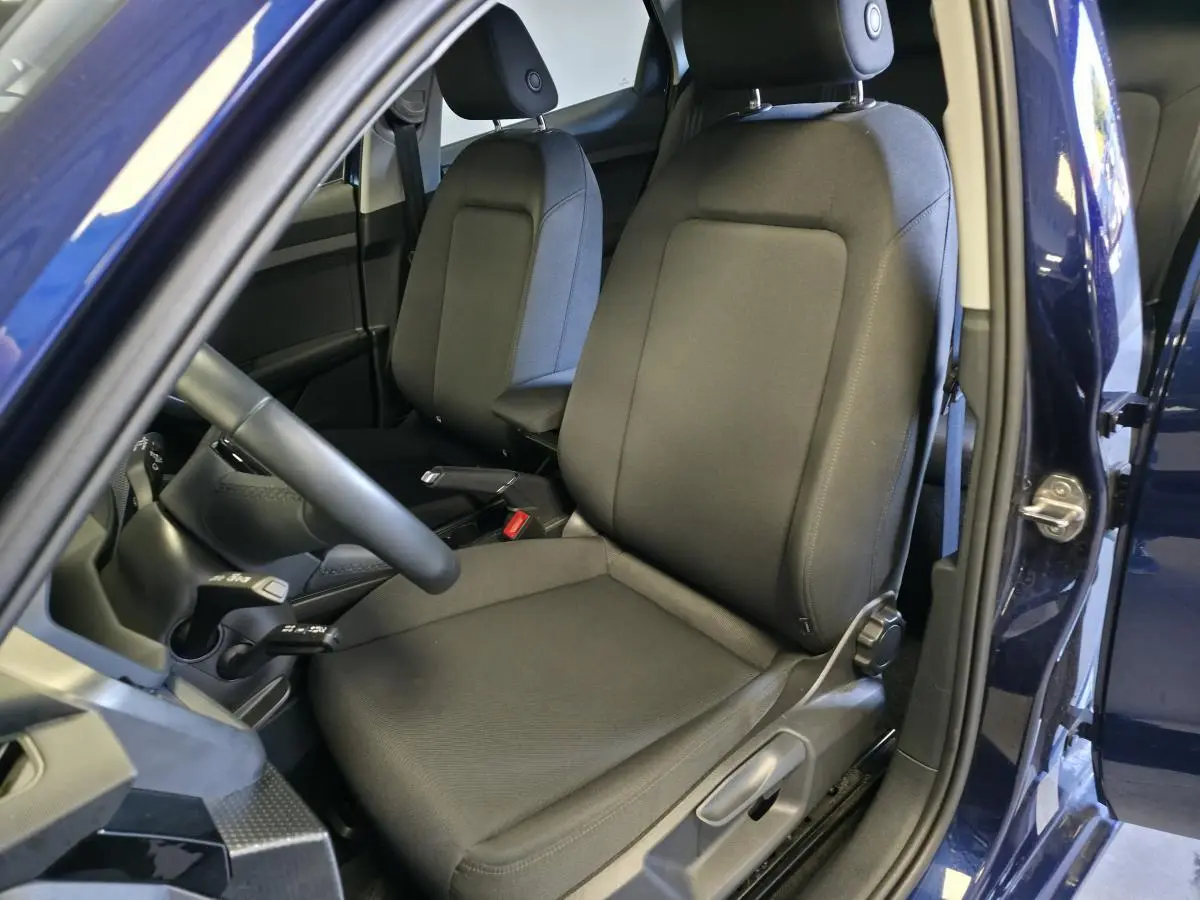 Vue intérieure côté conducteur de l'Audi A1 Sportback 2024 bleu, sièges sport en tissu noir et accoudoir central.