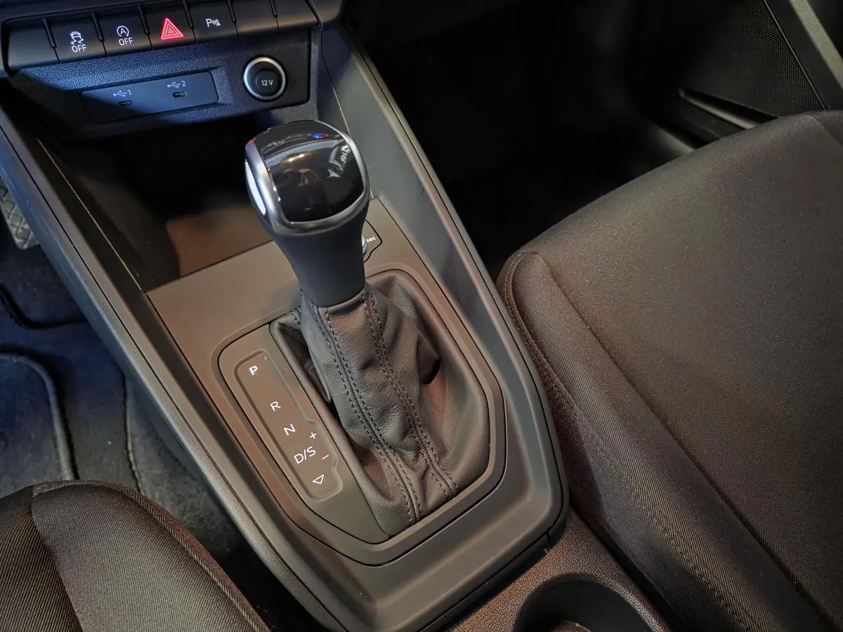 Gros plan sur la console centrale avec levier de vitesses automatique noir et sièges avant en tissu gris dans une Audi A1 Sportback.