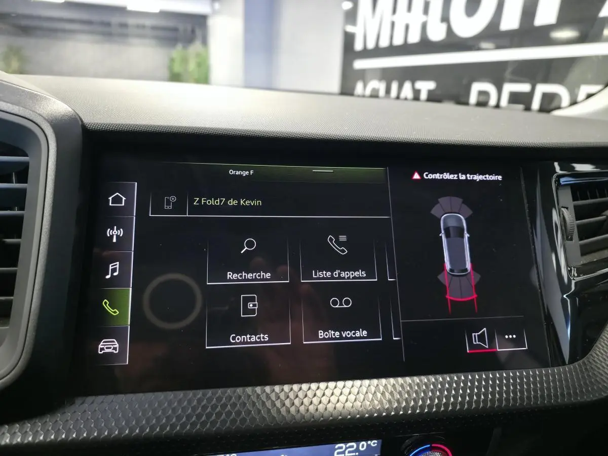 Écran tactile central de l’Audi A1 2024 affichant le menu appels et l’aide au stationnement, avec finition noire texturée.
