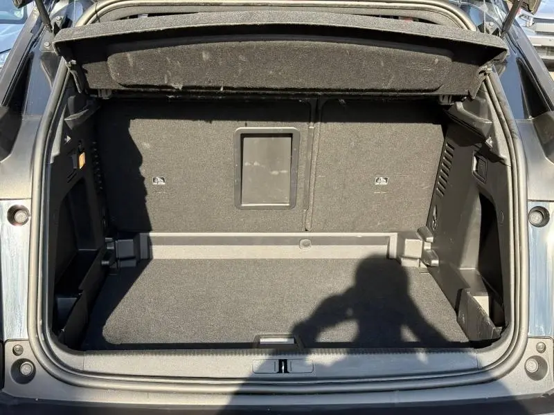 Coffre ouvert du Peugeot 3008 2024 en bleu Célèbes, vue de l'arrière, montrant un espace de chargement spacieux et bien fini.