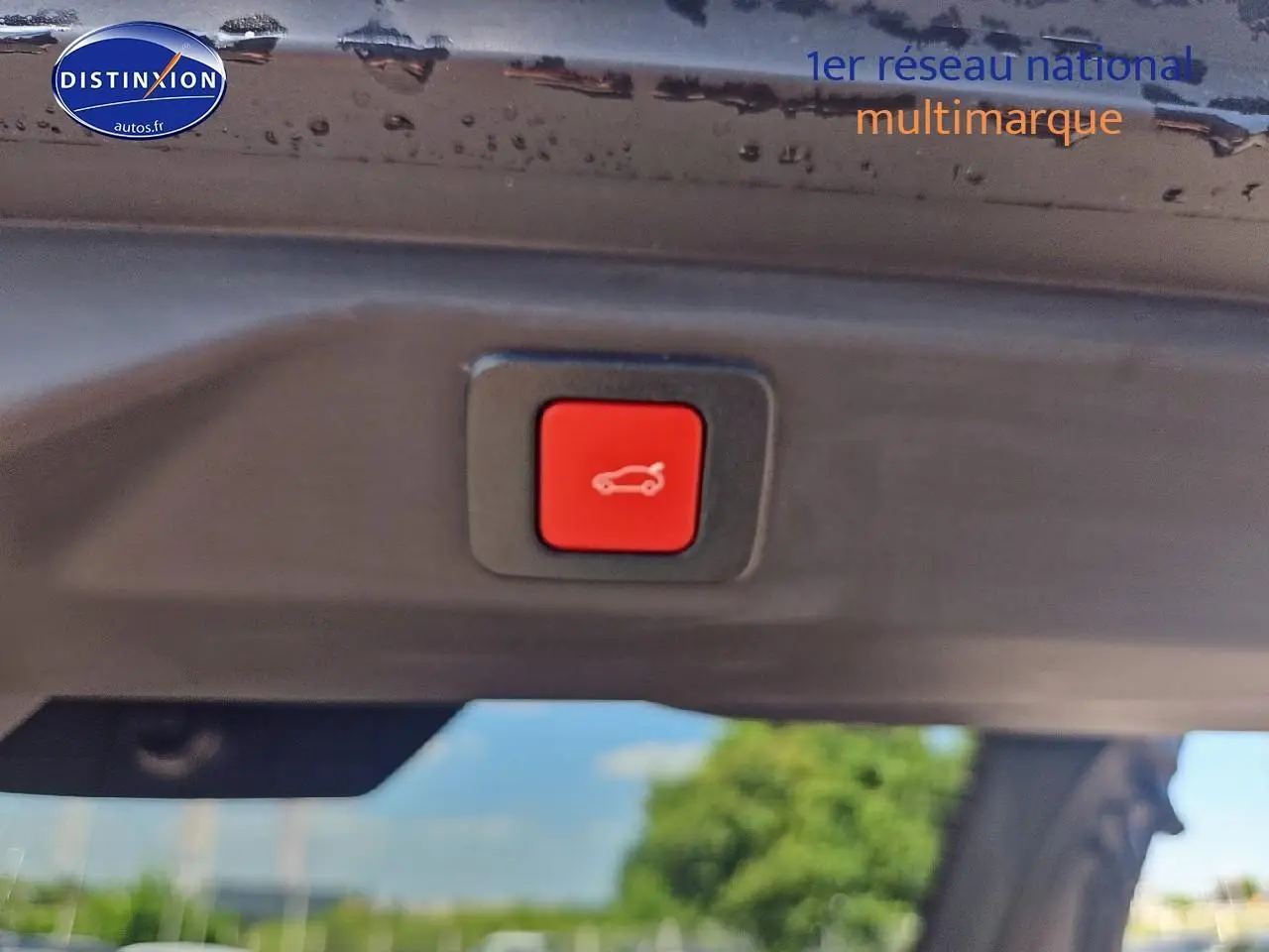 Bouton rouge d'ouverture électrique du coffre visible sous le hayon noir d'un Peugeot 3008 hybride 2025.