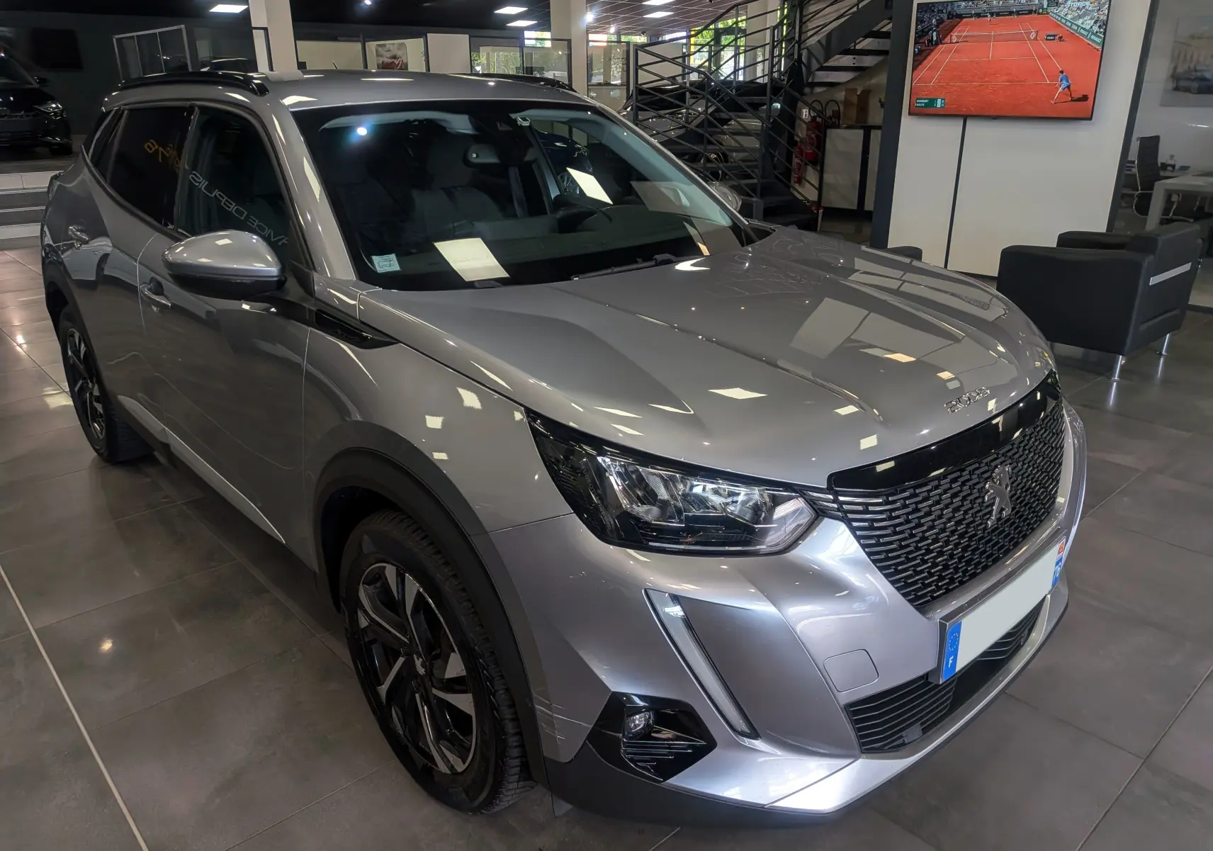 Peugeot 2008 gris Artense vue 3/4 avant droit en showroom, soulignant sa calandre noire et ses optiques LED.