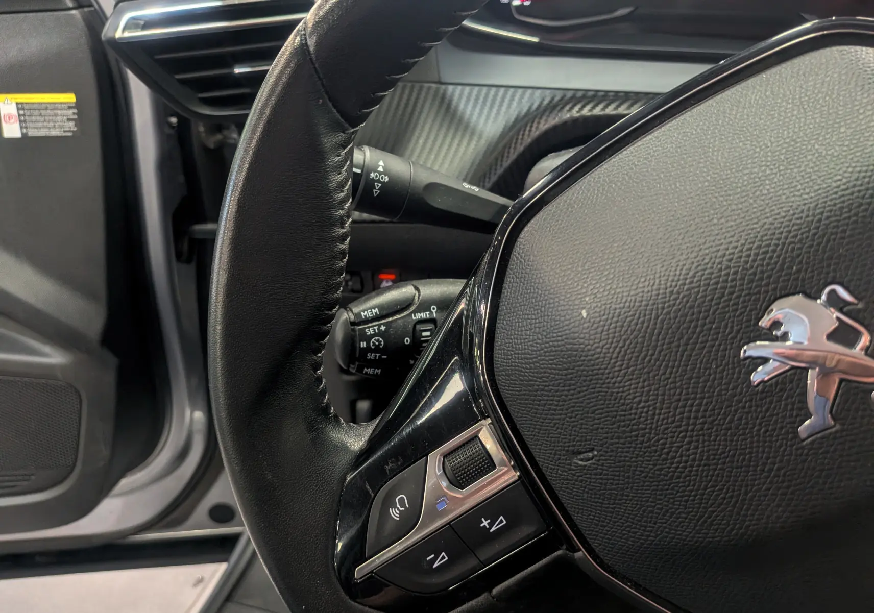 Gros plan sur le volant cuir noir du Peugeot 2008 gris Artense, avec commandes intégrées et tableau de bord partiel visible.
