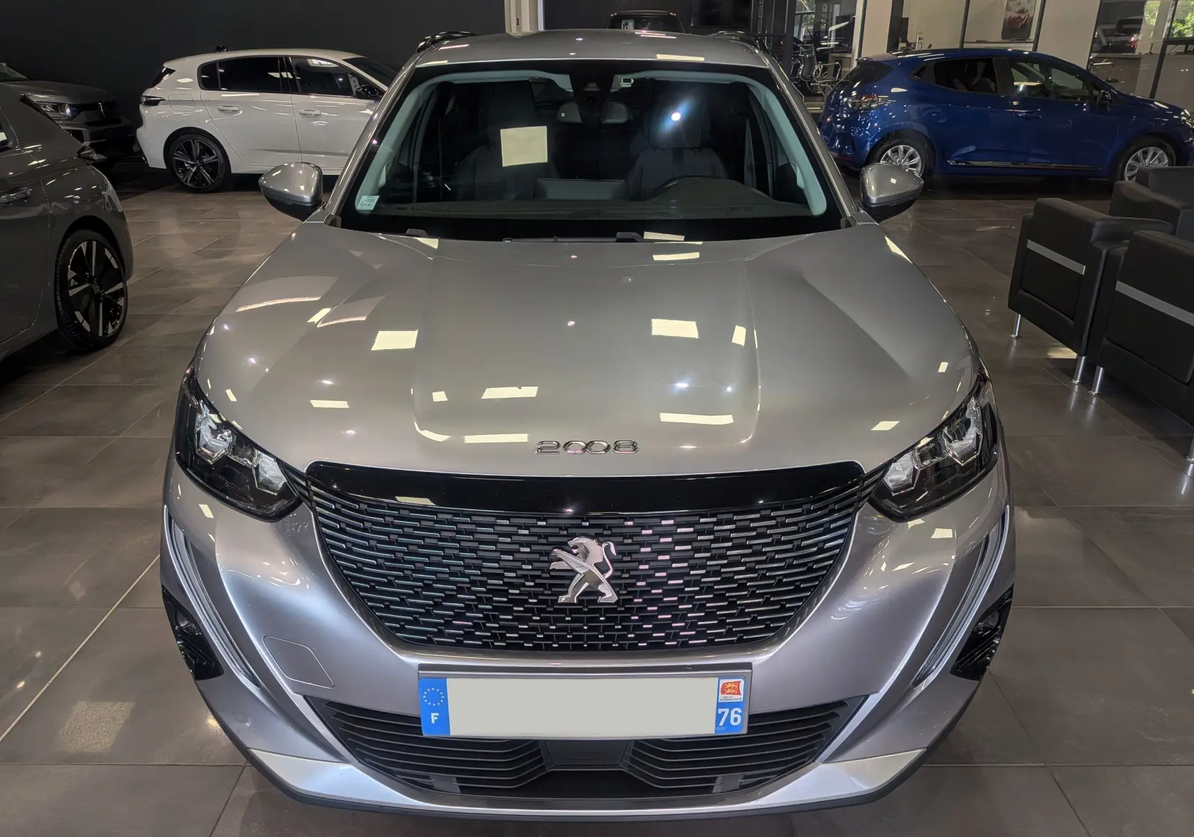 Vue frontale d'un Peugeot 2008 gris Artense 2021 avec calandre noire et logo lion au centre, en showroom.