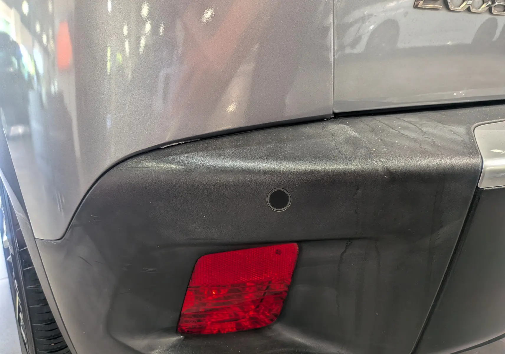 Détail du pare-chocs arrière droit gris Artense d’une Peugeot 2008 avec feu antibrouillard et capteur de recul.