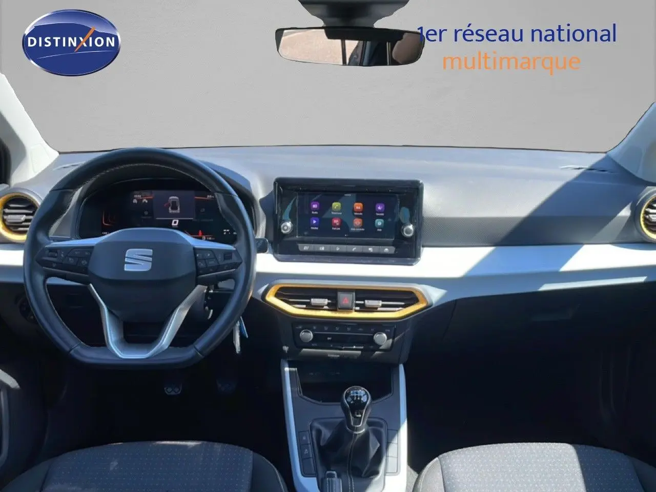 Vue intérieure avant du tableau de bord du SEAT Arona 2025, volant cuir, écran tactile et détails jaunes autour des aérateurs.