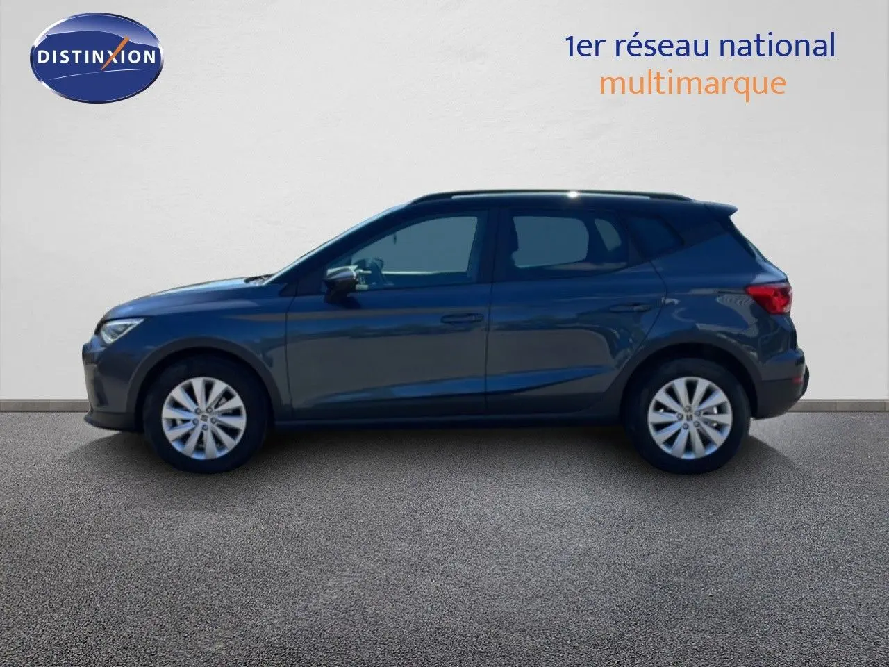 Vue latérale gauche d'un SEAT Arona 2025 gris Magnetic Metal avec toit noir, posé sur sol gris devant un mur blanc.