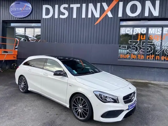 Vue 3/4 avant droite d'une Mercedes CLA Shooting Brake 200D WhiteArt blanche avec jantes AMG bicolores devant un bâtiment Distinxion.