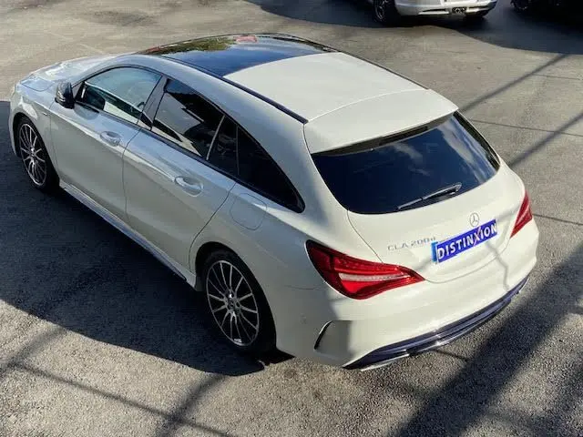 Vue 3/4 arrière droite d'une Mercedes CLA Shooting Brake 200D blanche avec toit panoramique et jantes AMG noires.
