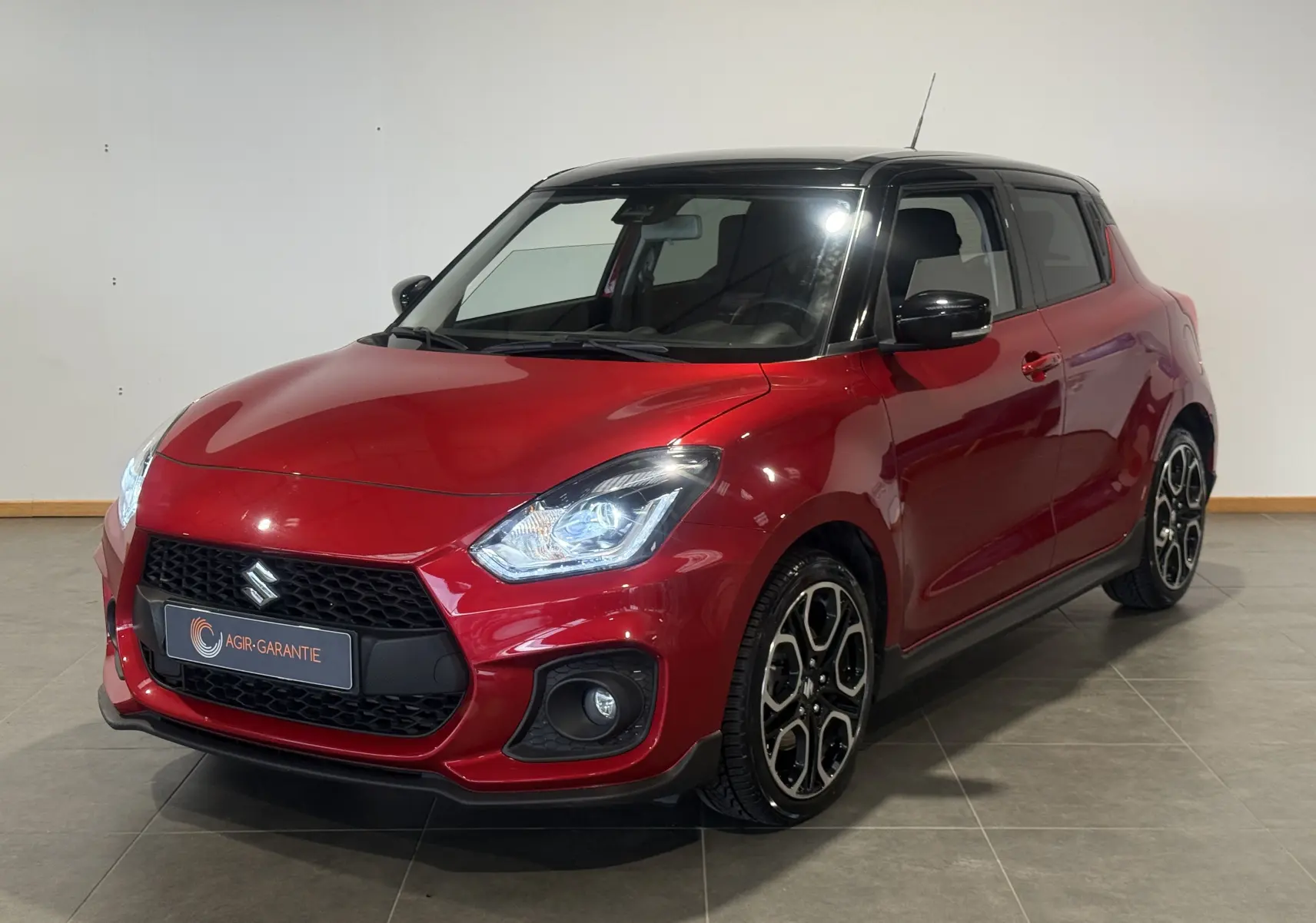 Vue 3/4 avant droite d'une Suzuki Swift Sport rouge 2022 avec toit noir et jantes alliage distinctives.