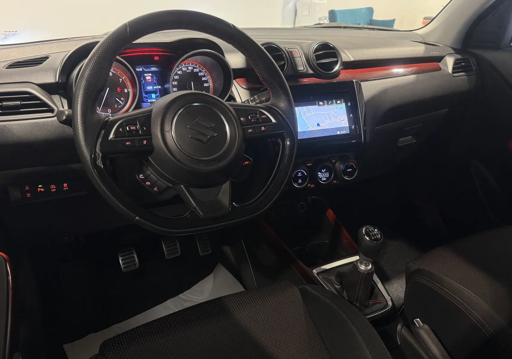 Vue intérieure côté conducteur du Suzuki Swift Sport 2022, tableau de bord noir avec touches rouges et levier de vitesse manuel.