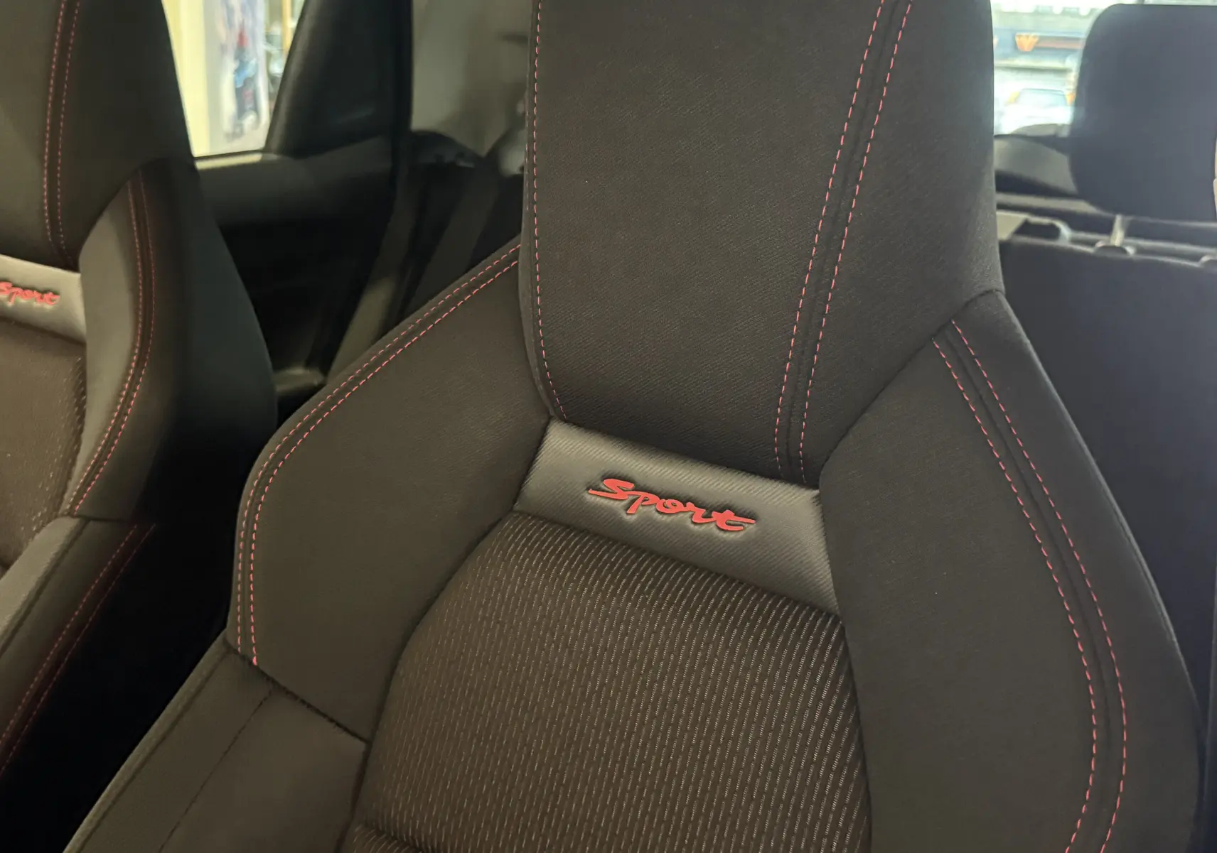 Gros plan sur le siège avant droit noir avec surpiqûres rouges et logo Sport rouge du Suzuki Swift Sport 2022.