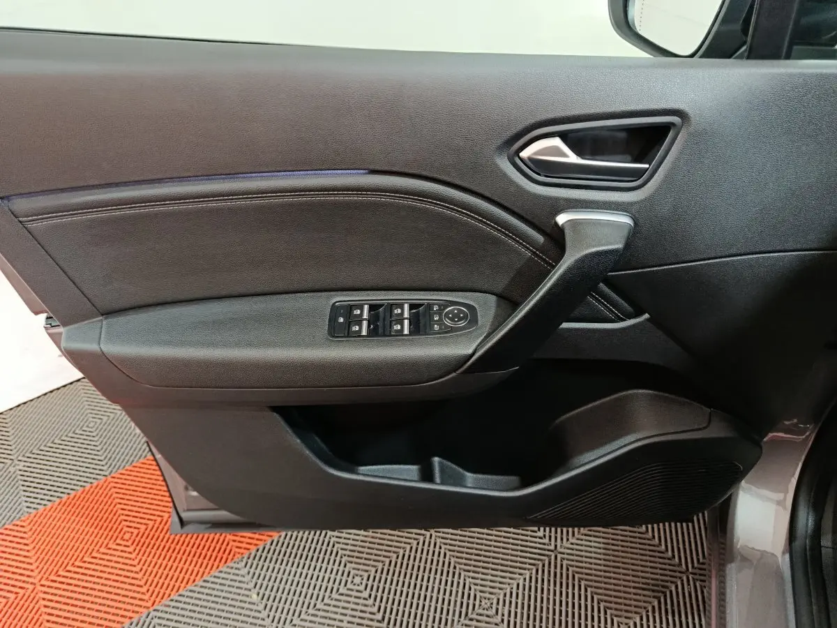 Vue intérieure côté gauche de la porte avant d’un Renault Captur gris foncé, avec commandes des vitres et poignée noire.