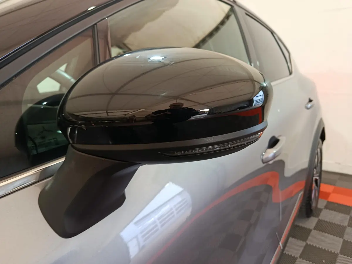Gros plan sur le rétroviseur noir côté gauche du Renault Captur gris foncé, avec partie avant du véhicule visible.