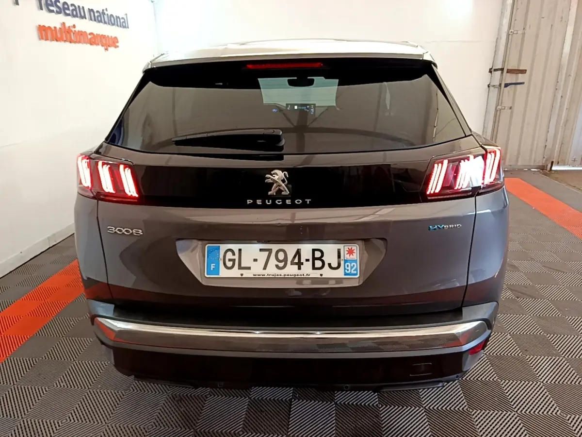 Vue arrière d'un Peugeot 3008 gris foncé hybride avec feux LED caractéristiques allumés en intérieur.