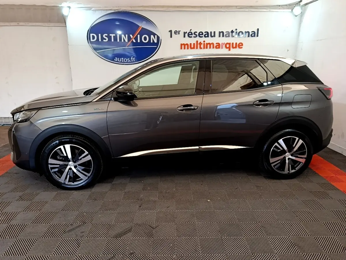 Profil côté gauche d’un Peugeot 3008 hybride rechargeable gris foncé, avec jantes alliage et toit blanc visible en intérieur showroom.