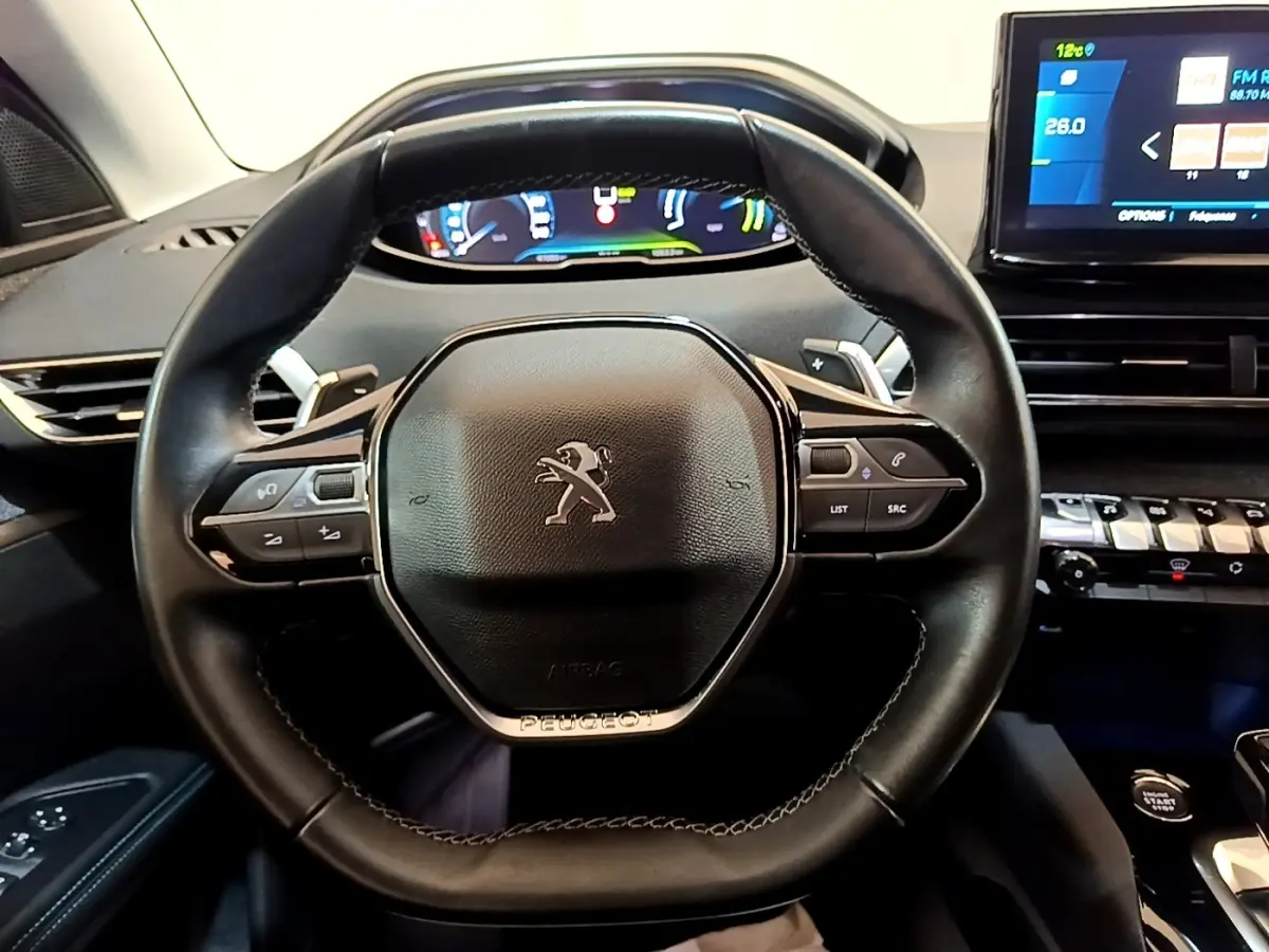 Vue rapprochée du volant cuir noir du Peugeot 3008 1.6 Hybrid 225, avec commandes multifonctions et tableau de bord digital.