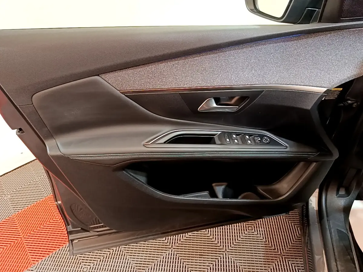 Vue intérieure côté gauche de la porte avant d’un Peugeot 3008 gris foncé avec commandes de vitres et poignée intégrée.