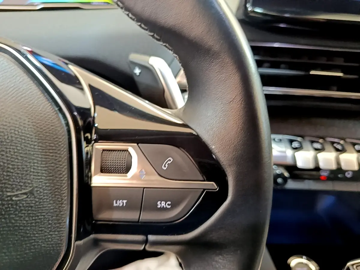 Gros plan sur les commandes gauche du volant cuir du Peugeot 3008 gris foncé, avec tableau de bord en arrière-plan.