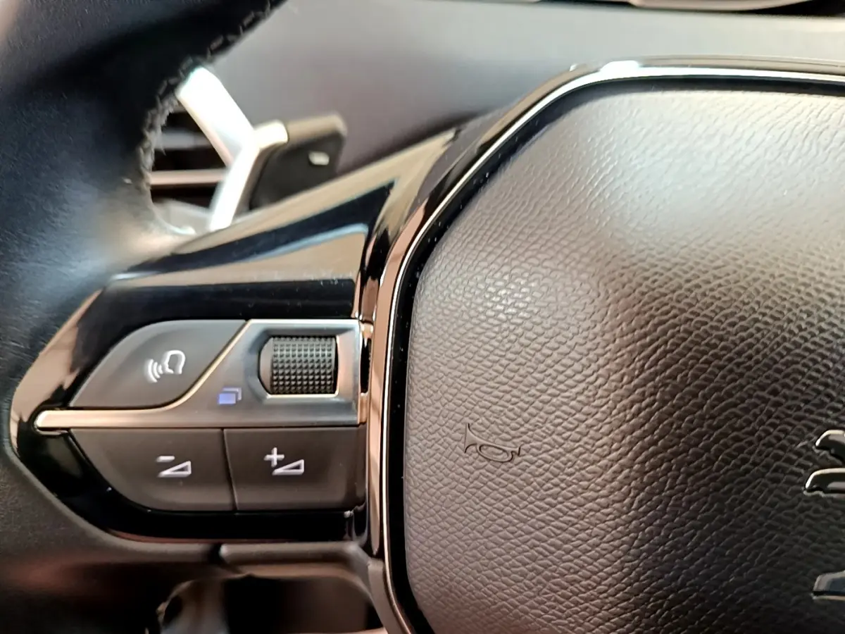 Gros plan sur les commandes gauche du volant cuir noir du Peugeot 3008 gris foncé hybride rechargeable 2022.