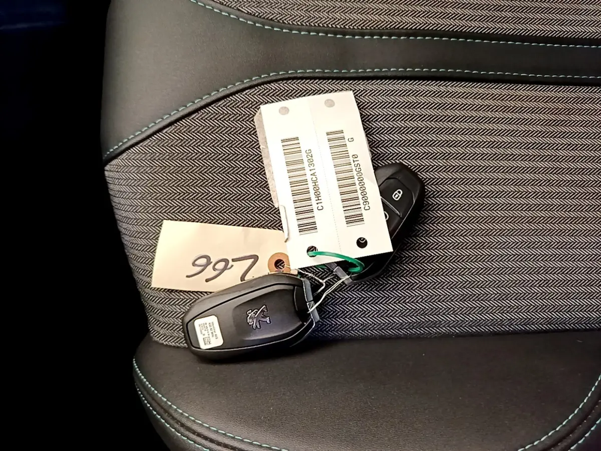 Gros plan sur la clé Peugeot posée sur un siège tissu gris foncé avec surpiqûres bleues.