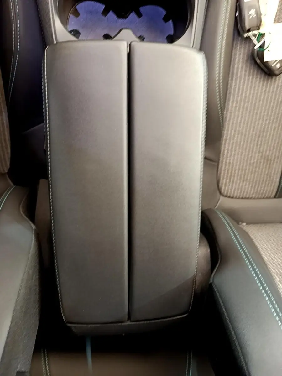 Vue plongeante sur l'accoudoir central noir avec surpiqûres bleues entre les sièges avant du Peugeot 3008 gris foncé.