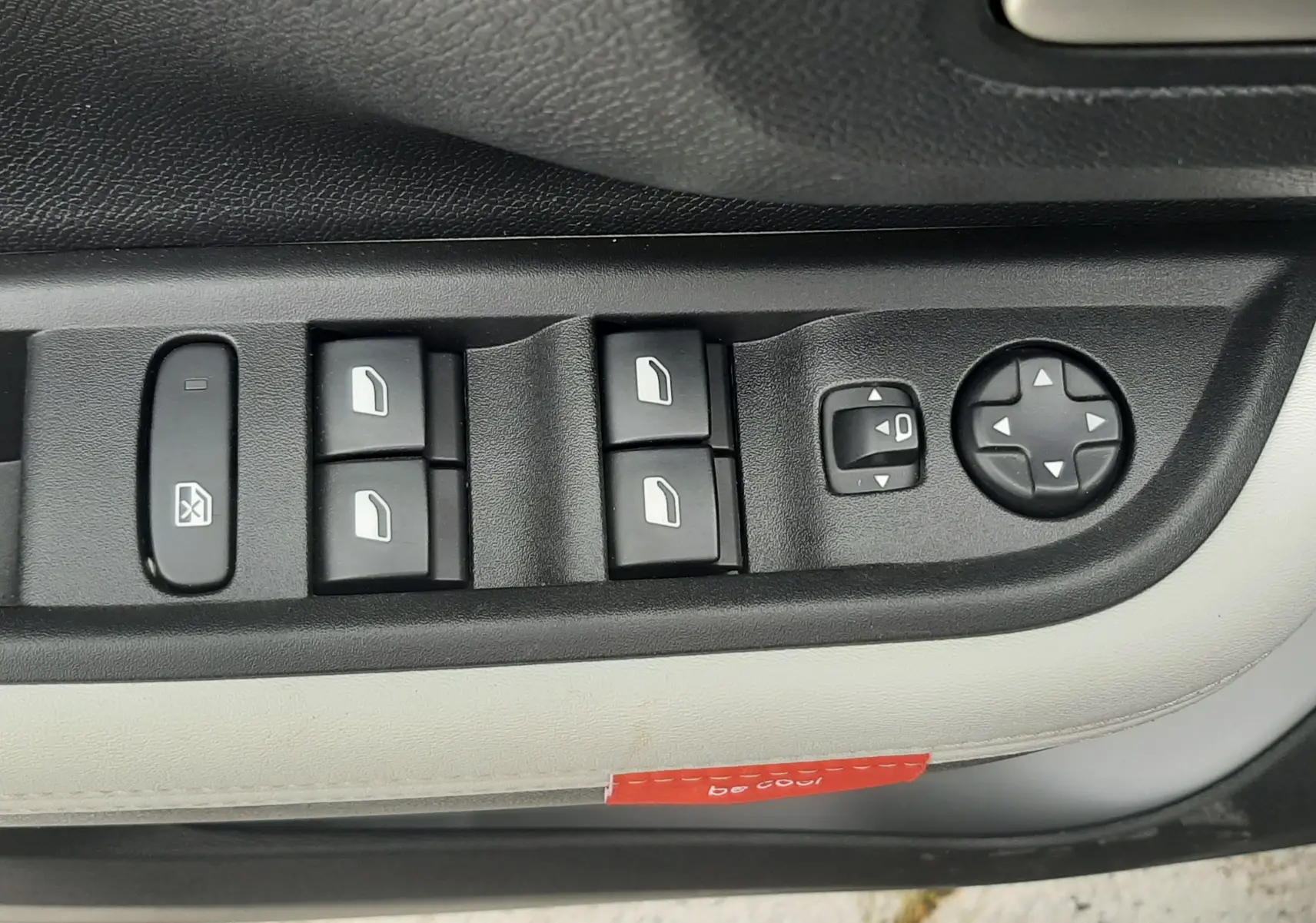 Gros plan sur les commandes électriques des vitres et rétroviseurs côté conducteur d'une Citroën C3 noir perla avec toit blanc.