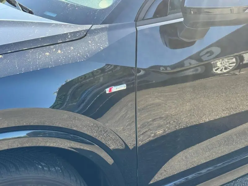 Gros plan sur l'aile avant gauche noire métallisée d'un Audi Q2 35 TFSI S line avec logo S tronic visible.