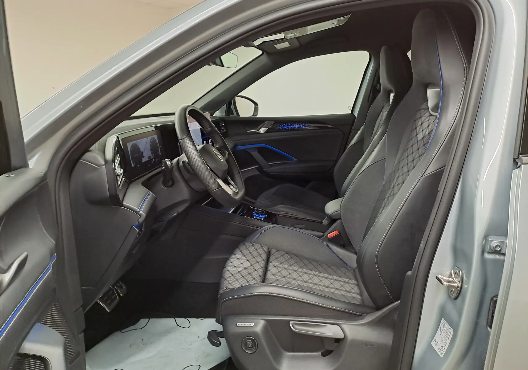 Intérieur avant droit du Volkswagen Tiguan 2.0 TDI 150 DSG7 R-LINE argent Dolomite avec sièges sport noirs et surpiqûres bleues.