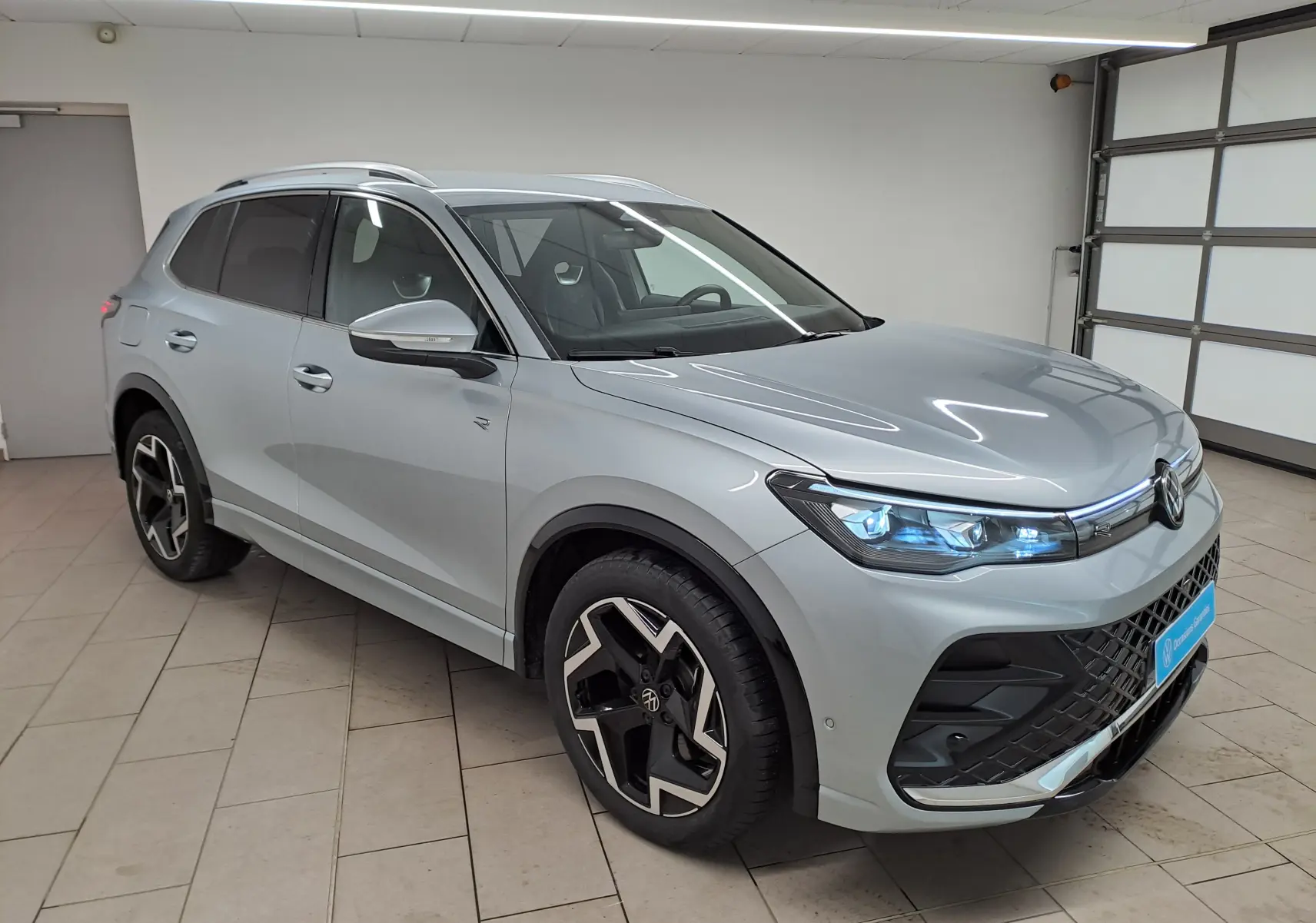 Volkswagen Tiguan 2.0 TDI R-Line argent Dolomite, vue 3/4 avant droit avec phares LED allumés en intérieur.