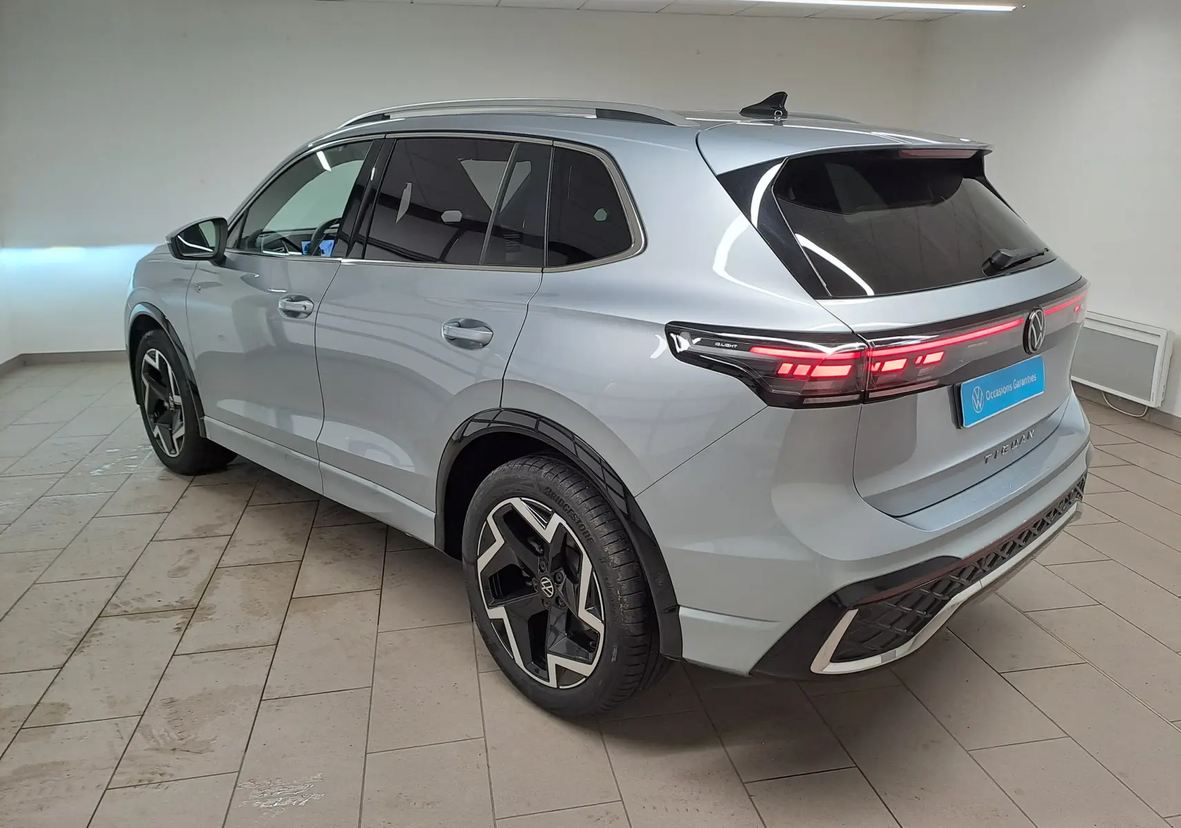 Volkswagen Tiguan 2.0 TDI R-Line argent Dolomite vu 3/4 arrière droit avec feux arrière LED allumés.