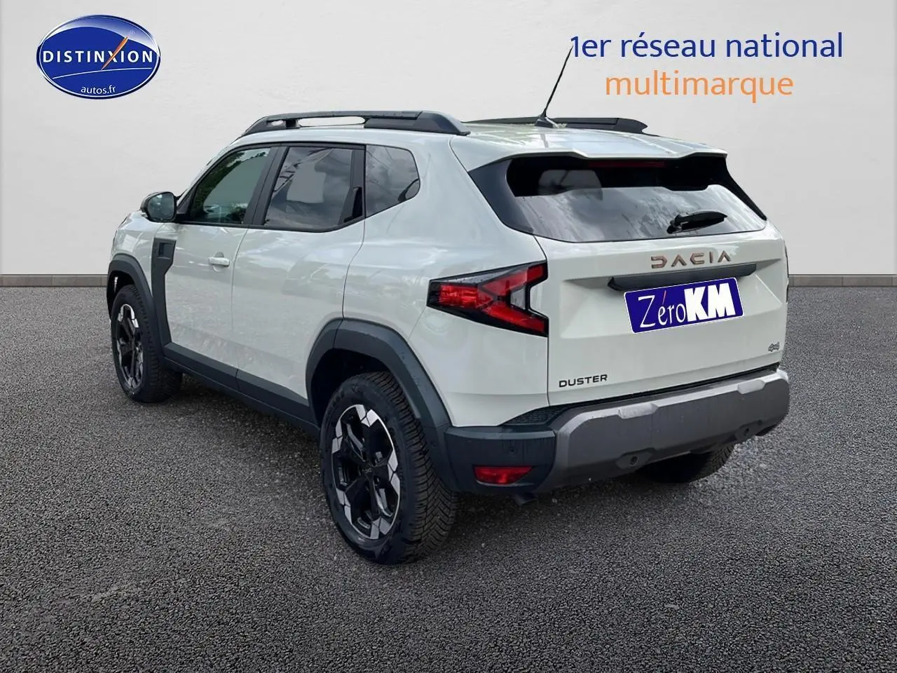 Vue 3/4 arrière droite du Dacia Duster 2025 couleur Sandstone avec barres de toit et jantes noires.