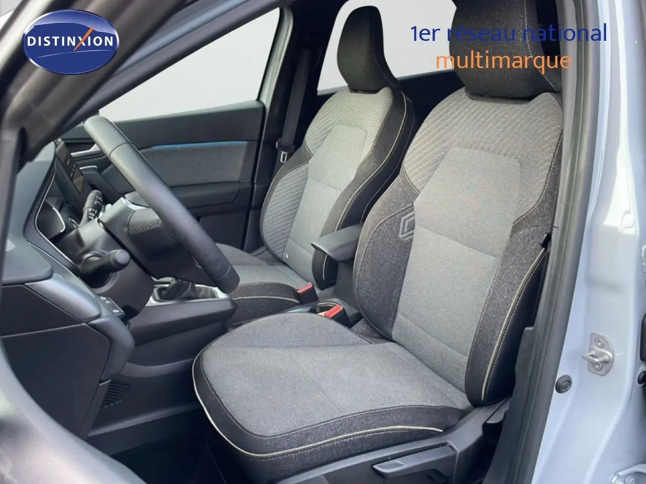 Vue intérieure côté conducteur du Renault Captur 2025, sièges tissu gris avec surpiqûres claires et volant cuir noir.