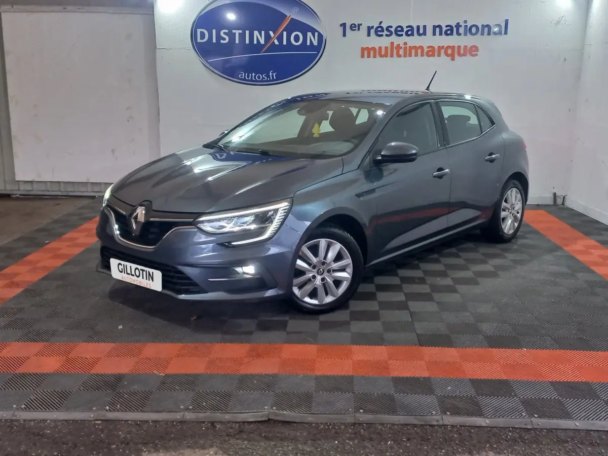 Renault Mégane Business TCe 115 gris foncé vue 3/4 avant droit, phares LED allumés en intérieur showroom.