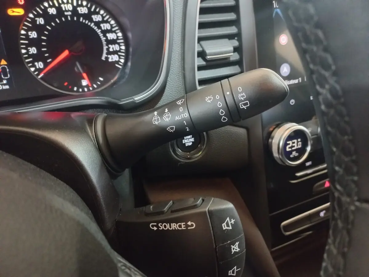 Gros plan sur les commandes au volant et tableau de bord d’une Renault Mégane Business gris foncé, avec affichage digital et bouton start.