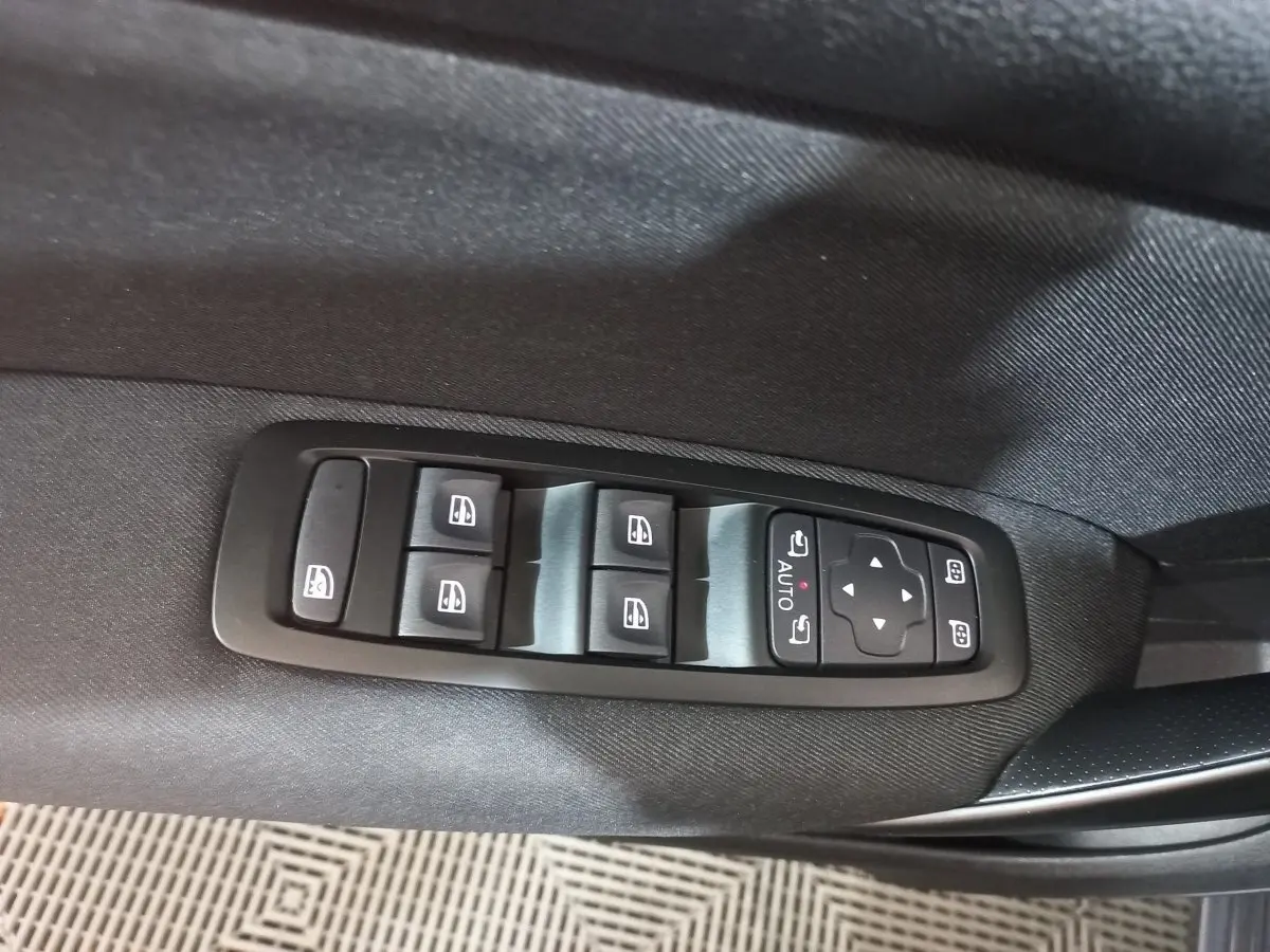 Vue rapprochée des commandes des vitres électriques et des rétroviseurs sur la porte côté conducteur d’une Renault Mégane gris foncé.