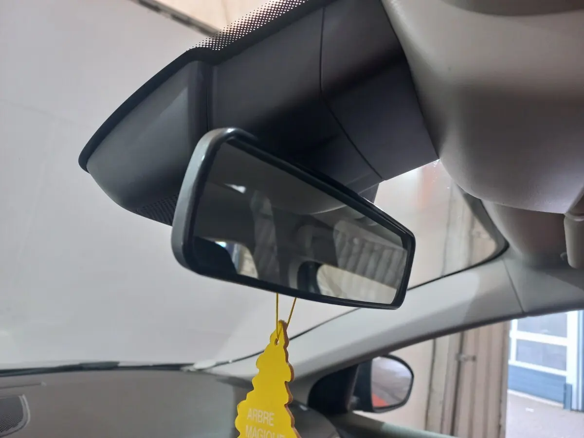 Vue intérieure centrée sur le rétroviseur intérieur d’une Renault Mégane gris foncé, avec un désodorisant jaune suspendu.